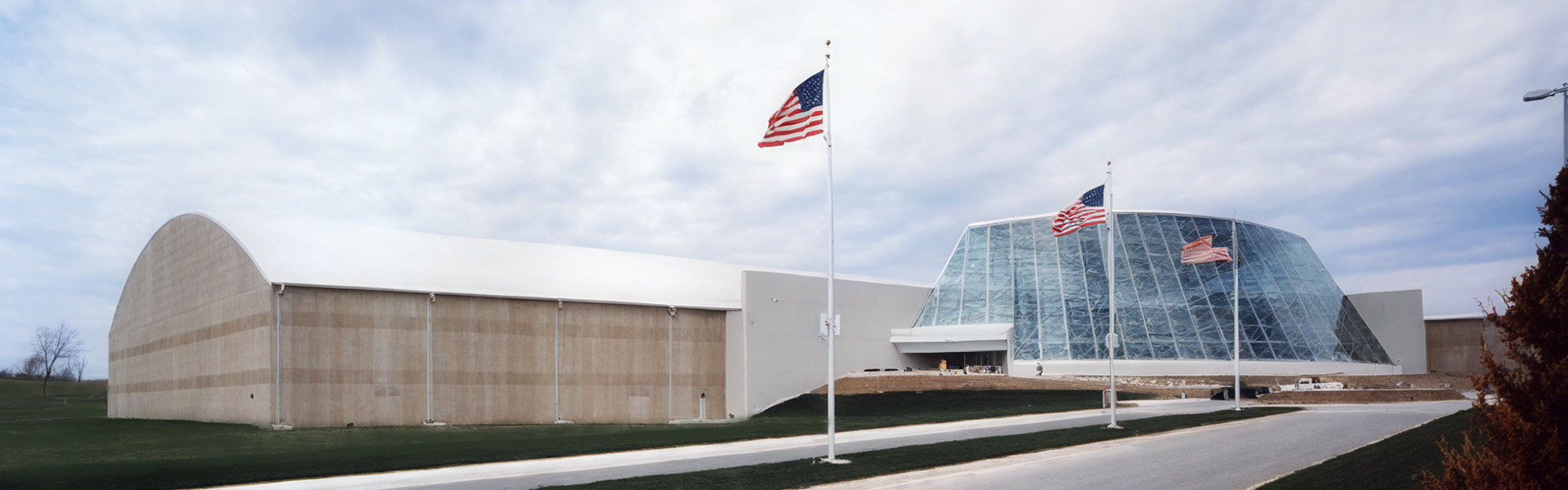 Museum complex with a curved metal hangar-style building and glass atrium entry